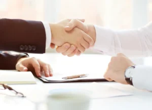 Two professionals shaking hands over supplier evaluation documents on a desk