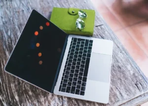 A silver laptop sits alone on a wooden bench in a public space, suggesting it was forgotten or misplaced. The laptop is closed, and there are no visible stickers or labels indicating ownership, highlighting the importance of labeling personal property for easy identification.