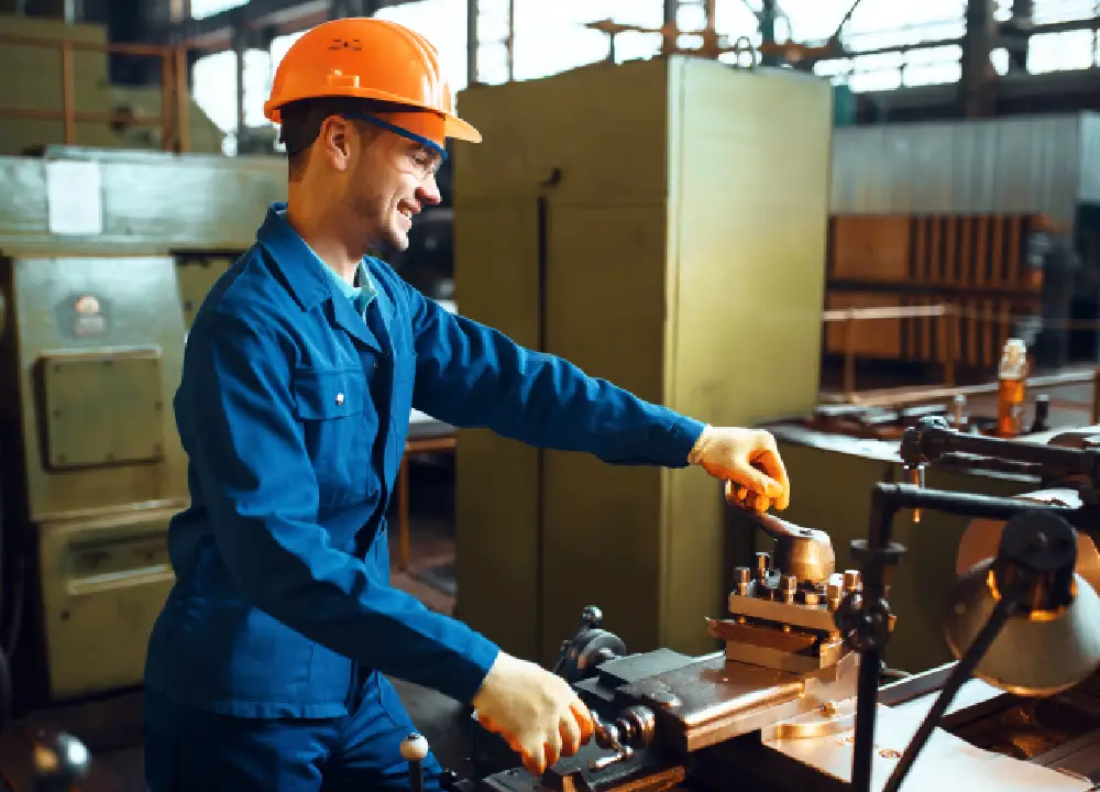 Industrial technician in safety gear operating a lathe machine in a manufacturing facility, focused on metalworking and precision engineering.

