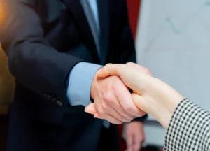Two professionals shaking hands over a desk with compliance documents, symbolizing a trusted API certification partnership.